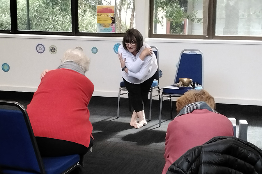 Two participants following instructor in seated yoga class