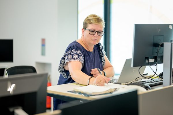 Woman sitting in front of computer and taking written notes in excel class